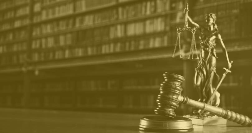 Statue of lady justice on desk of law office with legal books on shelf