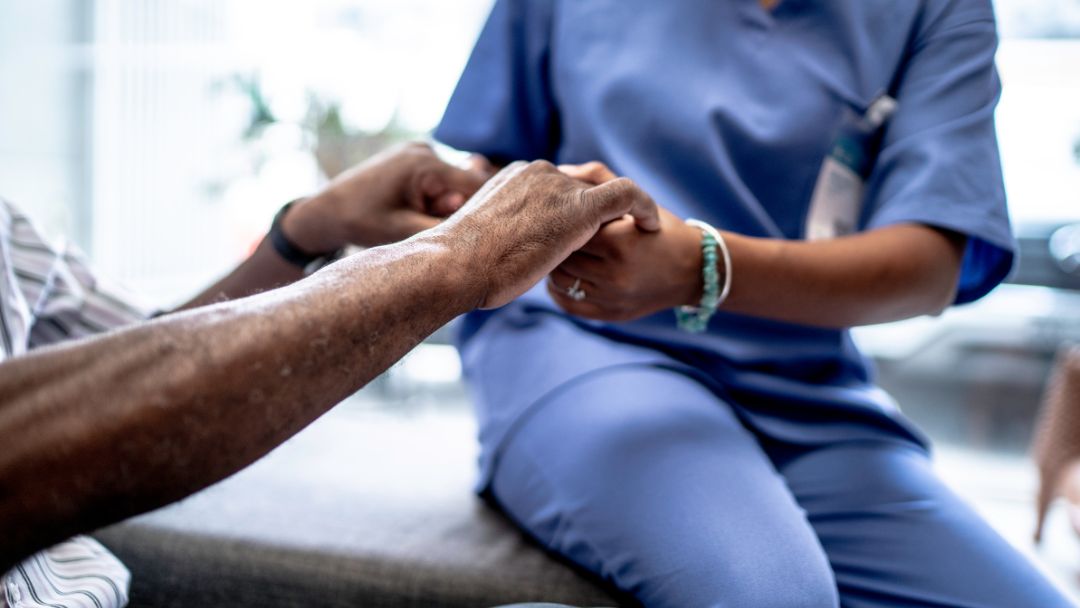 close up of nursing home caretacker holding hands of elderly woman sitting on a bed