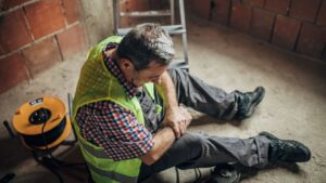 Construction worker on ground holding arm in pain after fall from a ladder