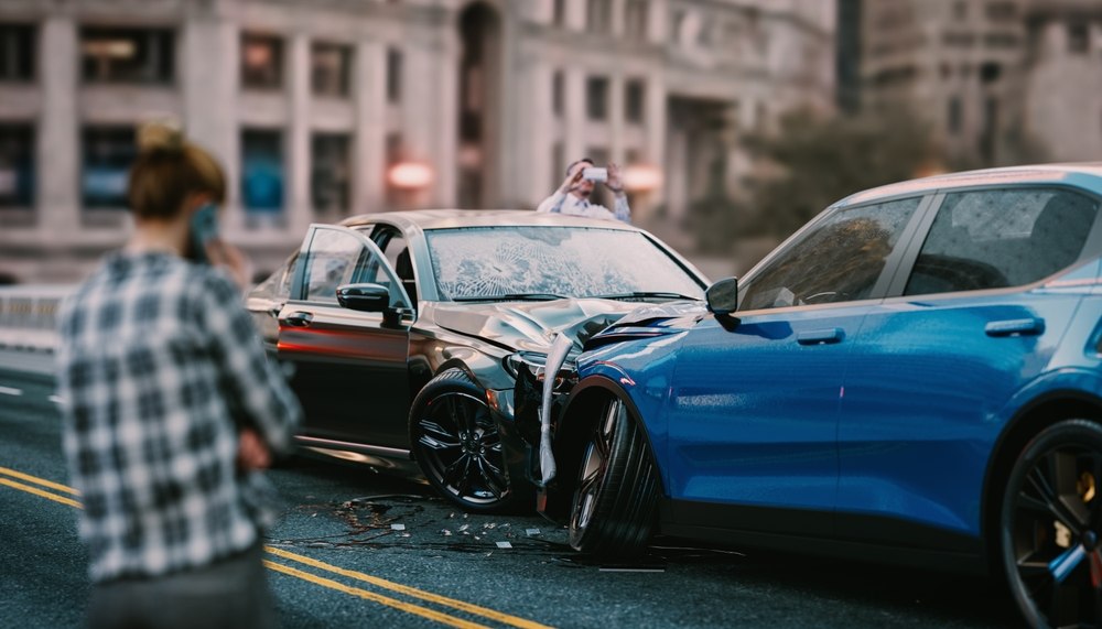 Man on the phone near a car accident scene with two damaged vehicles on a city street