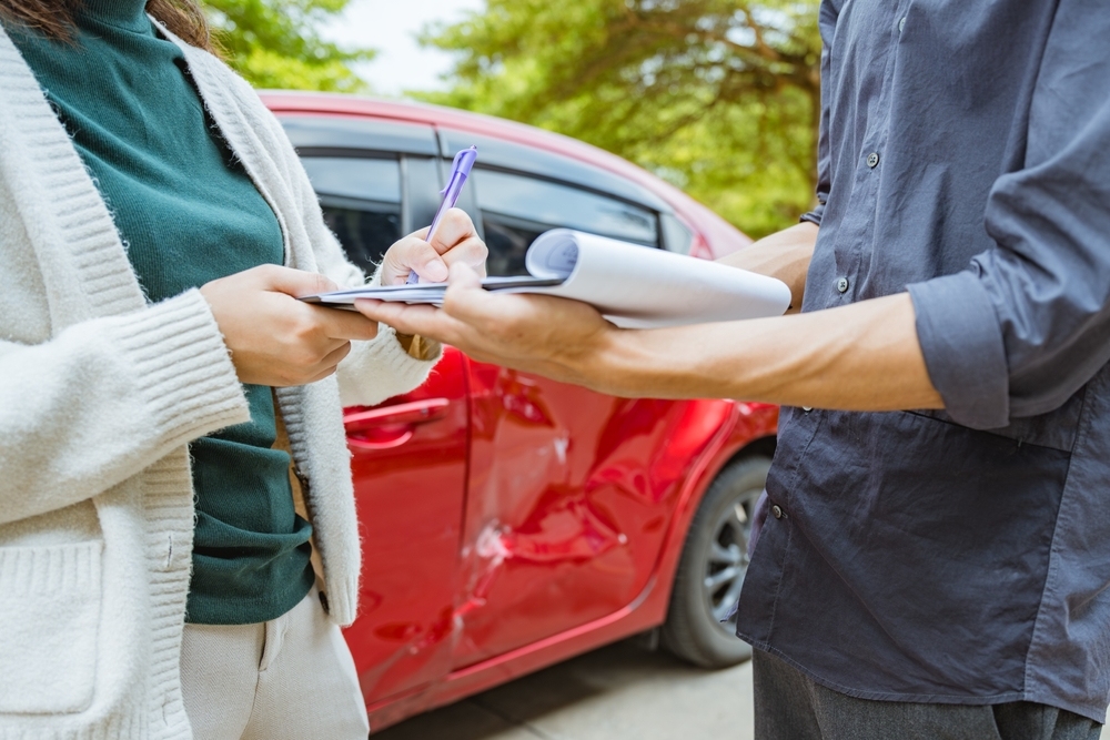 Two drivers exchanging insurance and contact information beside a damaged car after a Sand Springs accident