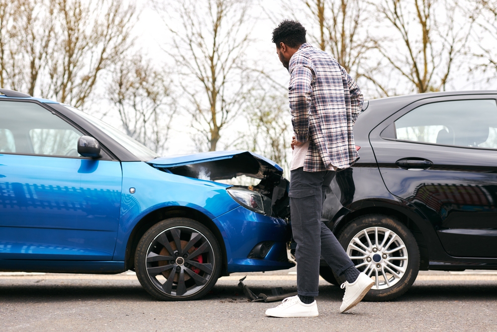 Man standing beside a blue car with damaged front end examining the aftermath of a Sand Springs collision