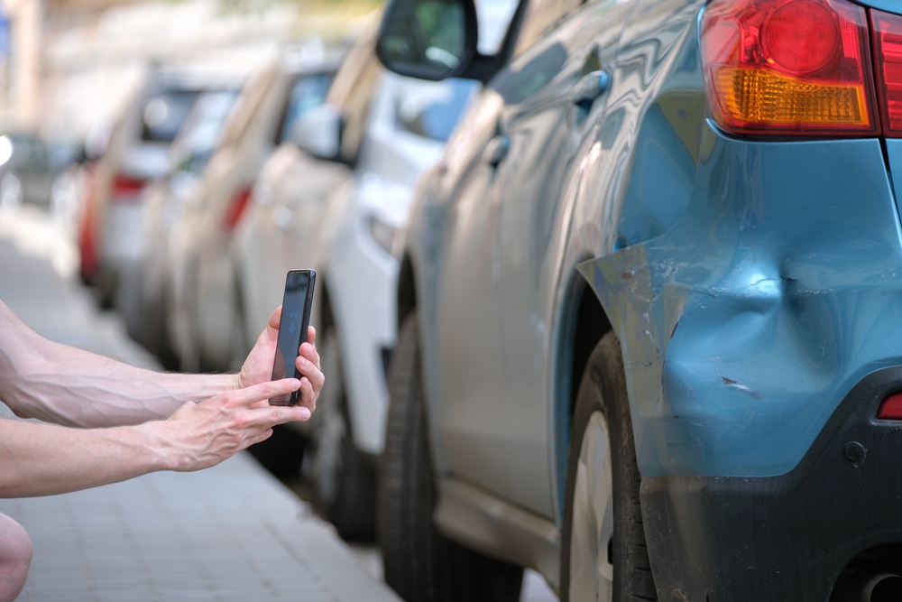 Driver taking photo evidence of damage to car after a hit-and-run accident