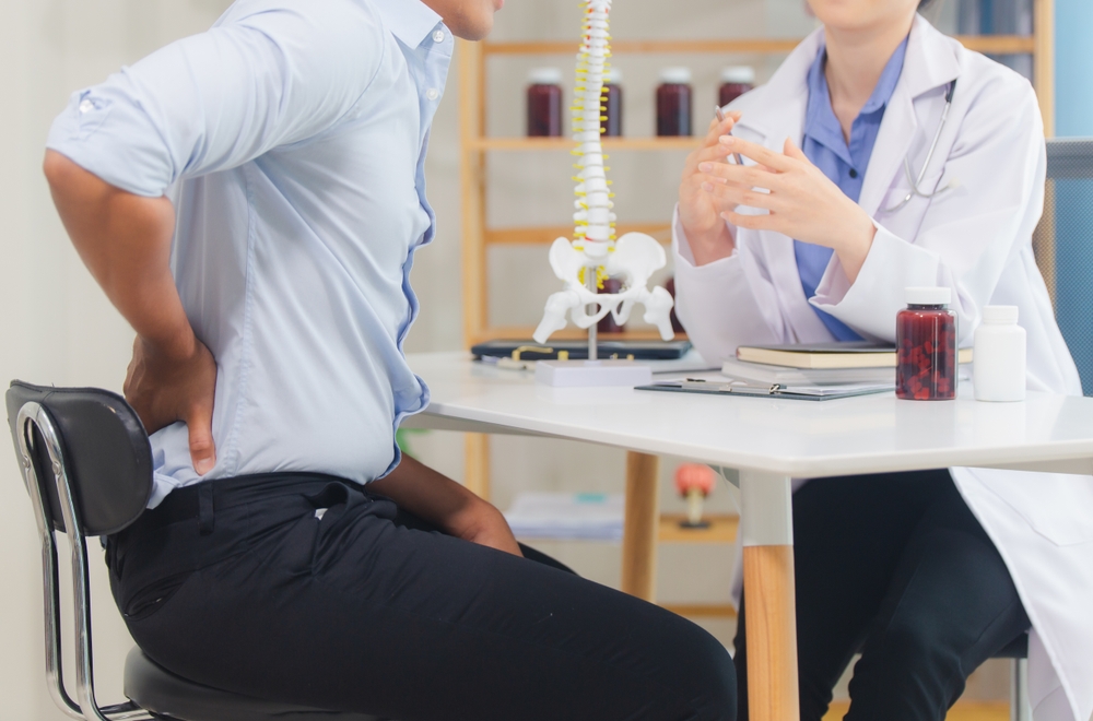 An orthopedic doctor shows a spinal model to a patient in a human spinal hospital. Diseases and disorders of the spinal cord, back pain, lumbar pain, orthopedic surgery, chiropractic, office syndrome