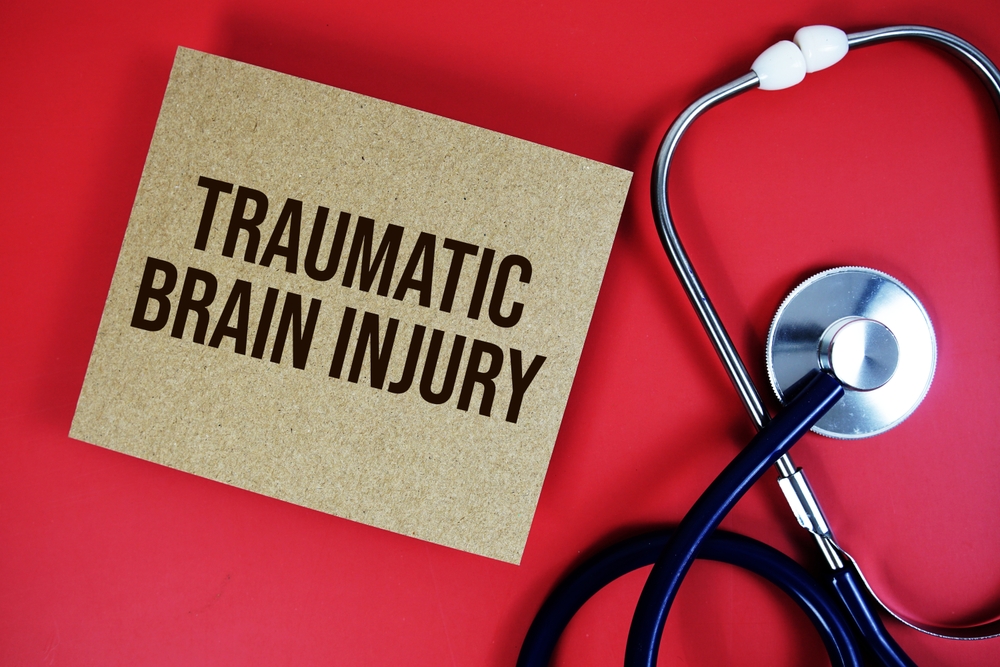 Traumatic Brain Injury text written on a paper card with a stethoscope on a red background