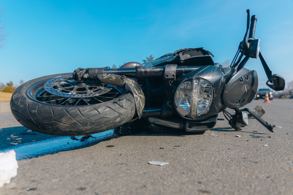 Black motorcycle with serious damage is on the asphalt. Accident close-up. Lost control and fell. Driving hazards. Collisions with another vehicle. Broken headlight and bent handlebars.